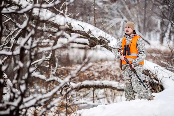 Manliga jägaren i kamouflage, beväpnad med ett gevär, stående i en sno — Stockfoto