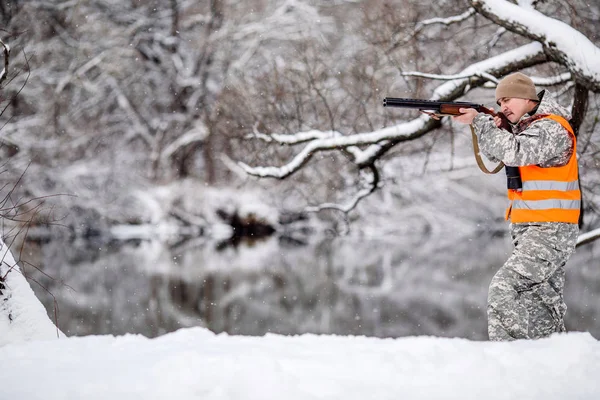 Caçador masculino em camuflagem, armado com uma espingarda, de pé em um sno — Fotografia de Stock