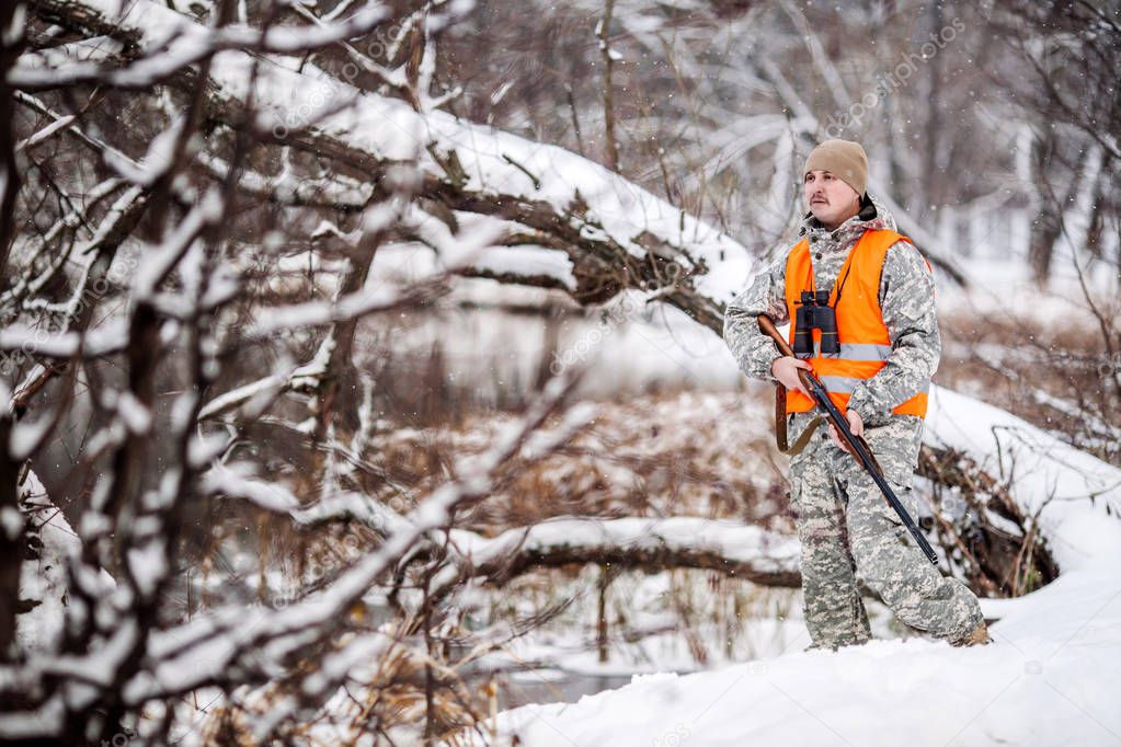 Male hunter in camouflage, armed with a rifle, standing in a sno