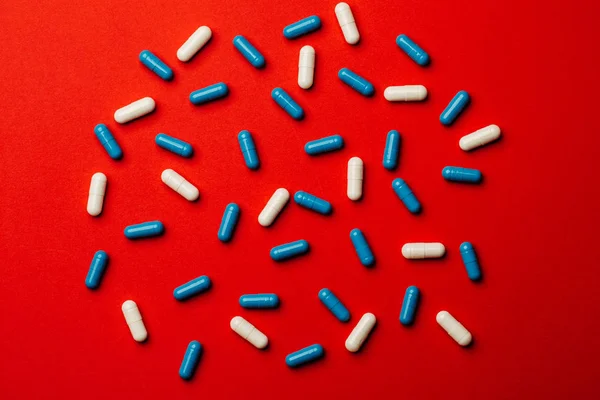 Pastillas azules y blancas cápsula sobre fondo rojo Medicina y phar —  Fotos de Stock