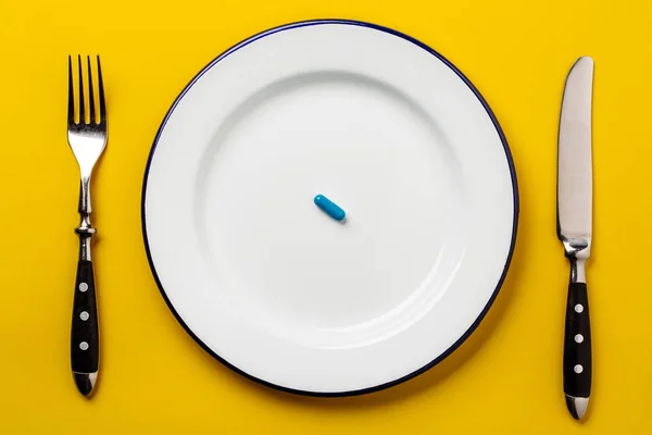 Blauwe pil op een witte plaat met vork en mes op een gele backg — Stockfoto