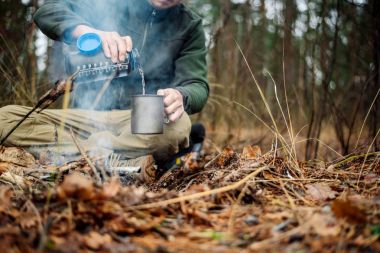 hunter pours water from a bottle into a metal mug. bushcraft, ad clipart