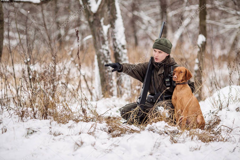 Male hunter in camouflage, armed with a rifle, standing in a sno