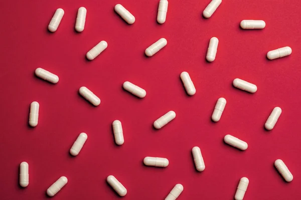 Muchas pastillas blancas sobre fondo rojo. Medicina y farmacia concep — Foto de Stock