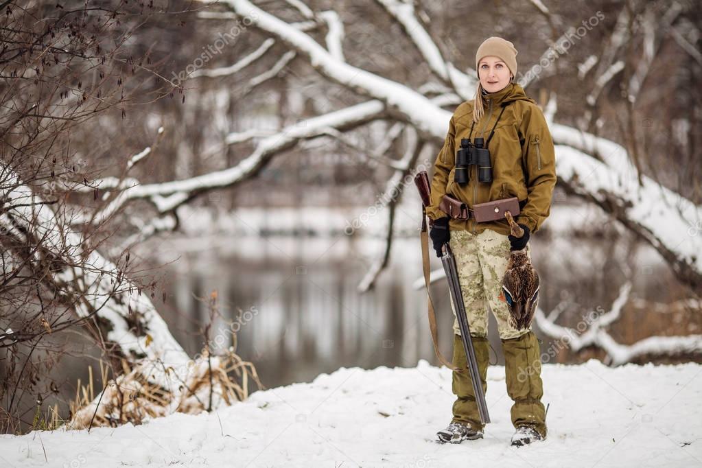 Female hunter in camouflage, armed with a rifle, standing in a s