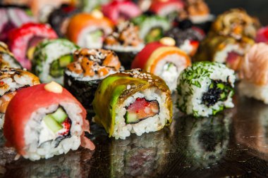 Suşi yemek çeşitli tür siyah arka plan üzerine servis. Plaka üzerinde balık ve pirinç lezzetli taze suşi rulo yakın çekim. Ahşap plaka bir restoranda sunulan suşi rulo