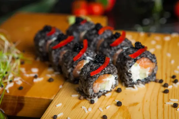 Berbagai jenis makanan sushi disajikan pada latar belakang hitam. Dekat sushi gulung segar lezat dengan ikan dan nasi di atas piring. Sushi rolls disajikan di piring kayu di sebuah restoran — Stok Foto