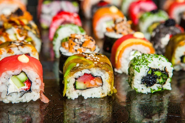 Varios tipos de comida de sushi servida sobre fondo negro. Primer plano de sabrosos rollos de sushi fresco con pescado y arroz en el plato. Rollos de sushi servidos en un plato de madera en un restaurante —  Fotos de Stock