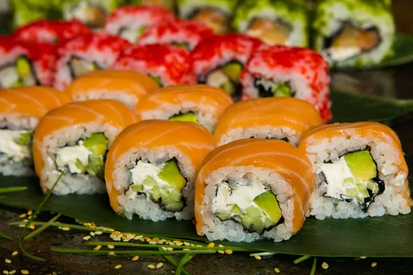 Verschiedene Arten von Sushi-Essen auf schwarzem Hintergrund serviert. Nahaufnahme von leckeren frischen Sushi-Rollen mit Fisch und Reis auf dem Teller. Sushi-Rollen auf einem Holzteller in einem Restaurant serviert — Stockfoto