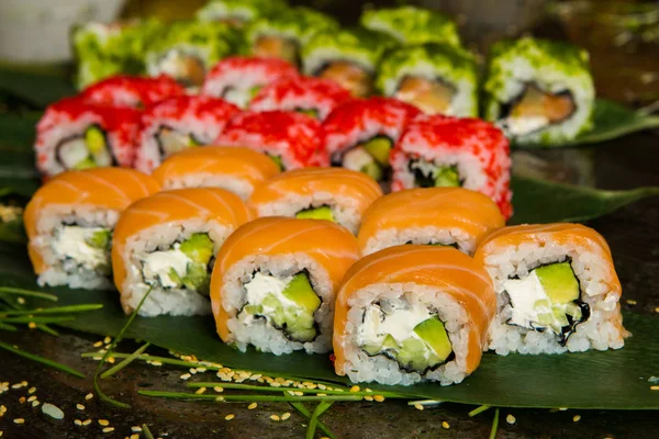 Vários tipos de comida de sushi servida em fundo preto. Close up de saborosos rolos de sushi frescos com peixe e arroz no prato. Rolos de sushi servidos em um prato de madeira em um restaurante — Fotografia de Stock