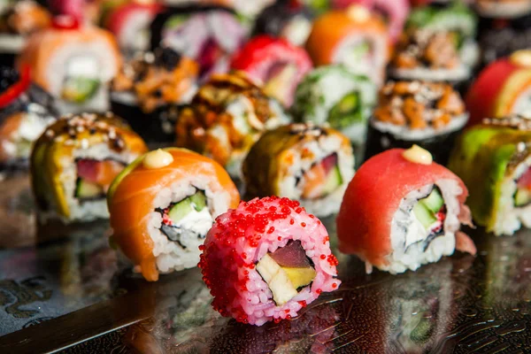 Varios tipos de comida de sushi servida sobre fondo negro. Primer plano de sabrosos rollos de sushi fresco con pescado y arroz en el plato. Rollos de sushi servidos en un plato de madera en un restaurante — Foto de Stock