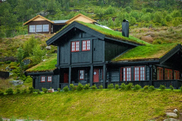 Tradicional casa de madera noruega de pie en un césped y montañas en el fondo. Típica casa noruega. típica casa noruega con césped en el techo . — Foto de Stock