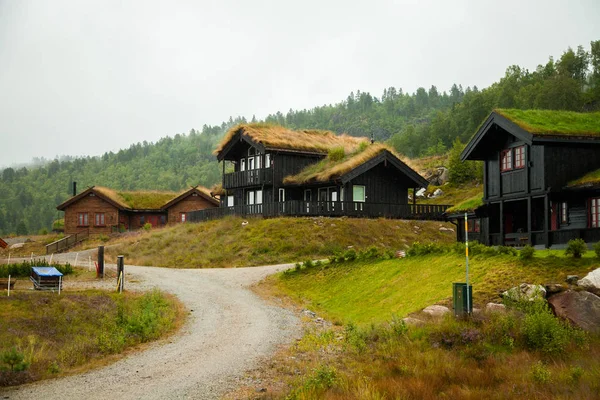 Tradicional casa de madera noruega de pie en un césped y montañas en el fondo. Típica casa noruega. típica casa noruega con césped en el techo . — Foto de Stock