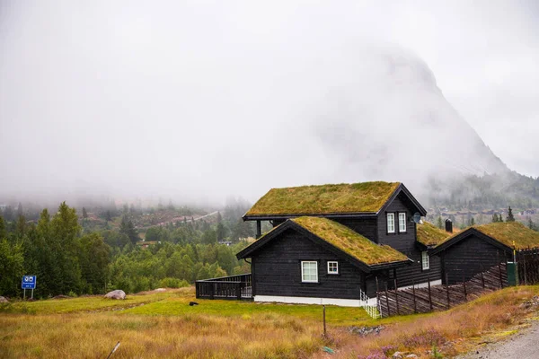 Tradicional casa de madera noruega de pie en un césped y montañas en el fondo. Típica casa noruega. típica casa noruega con césped en el techo . — Foto de Stock