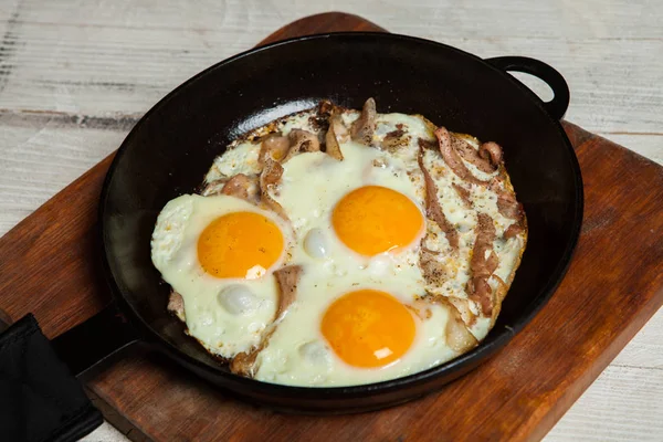 Fried eggs in a frying pan with becon. Fried eggs with bacon in a pan seasoned with herbs and pepper