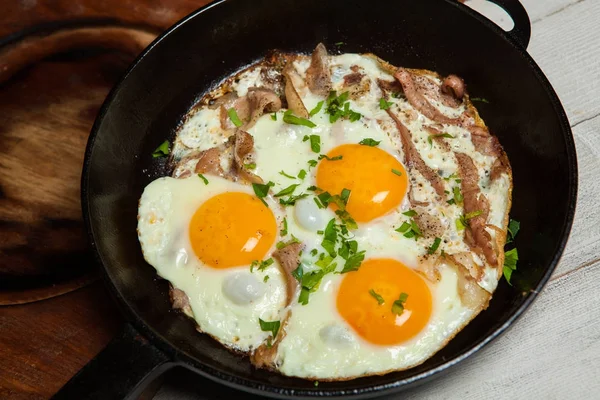 Fried eggs in a frying pan with becon. Fried eggs with bacon in a pan seasoned with herbs and pepper