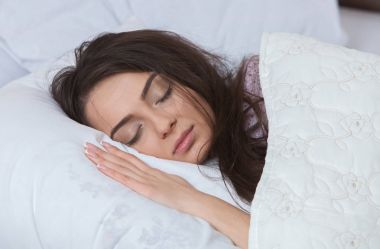 Kız evde beyaz bir yatakta uyuyor. Yatakta evde, üstten görünüm beyaz keten üzerinde pijama içinde uyuyan genç kadın.