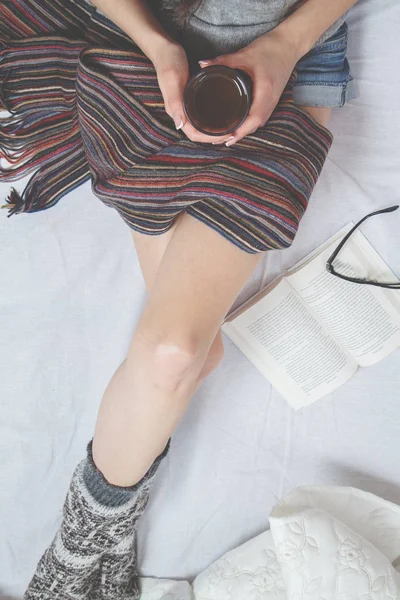 Beautiful Legs close-up in Bed. Woman is Drinking Tea and Reading a Book. Girl Sitting on a Bed in Woolen Socks. Beautiful Woman no Face and Legs. Attractive Model Wears Woolen Socks