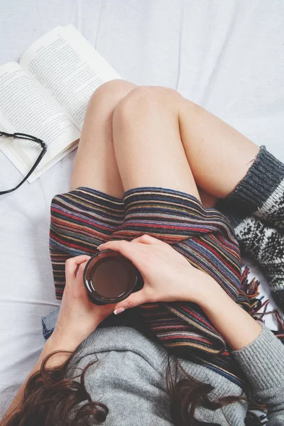 Beautiful Legs close-up in Bed. Woman is Drinking Tea and Reading a Book. Girl Sitting on a Bed in Woolen Socks. Beautiful Woman no Face and Legs. Attractive Model Wears Woolen Socks