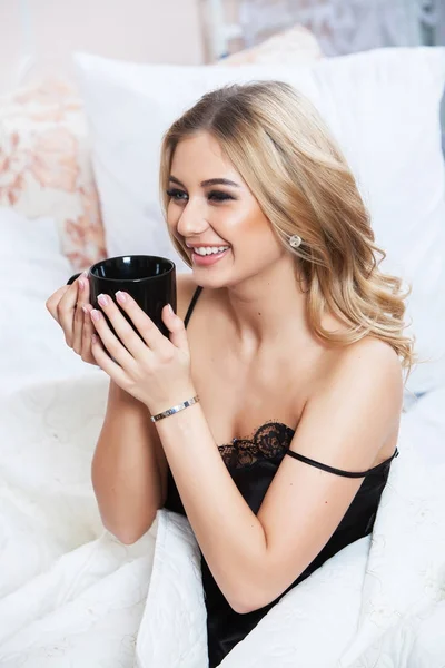 Relaxed woman lying in bed with cup of tea. Young beautiful woman awaking in light room