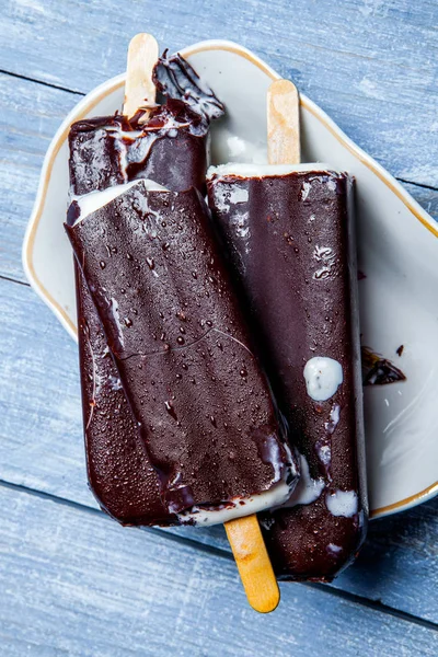 Chocolate ice cream pops on a blue wooden background. Chocolate ice cream on a rusty background. Eskimo ice cream on stick.