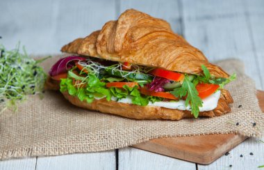 Kruvasan sandviç üzerinde ahşap kurulunda görev yapmaktadır. Kruvasan yumurta, eritilmiş peynir, maydanoz, tavuk jambon, füme somon ile