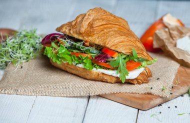 Kruvasan sandviç üzerinde ahşap kurulunda görev yapmaktadır. Kruvasan yumurta, eritilmiş peynir, maydanoz, tavuk jambon, füme somon ile