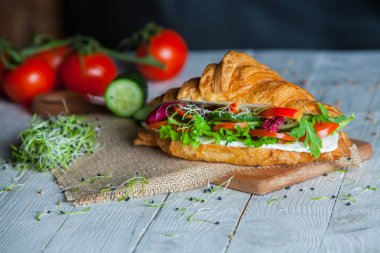 Kruvasan sandviç üzerinde ahşap kurulunda görev yapmaktadır. Kruvasan yumurta, eritilmiş peynir, maydanoz, tavuk jambon, füme somon ile