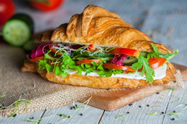 Kruvasan sandviç üzerinde ahşap kurulunda görev yapmaktadır. Kruvasan yumurta, eritilmiş peynir, maydanoz, tavuk jambon, füme somon ile