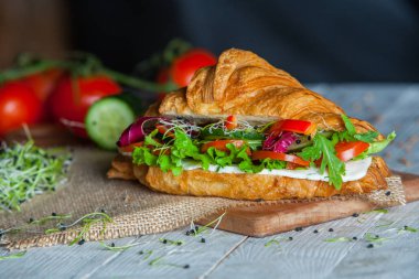 Kruvasan sandviç üzerinde ahşap kurulunda görev yapmaktadır. Kruvasan yumurta, eritilmiş peynir, maydanoz, tavuk jambon, füme somon ile