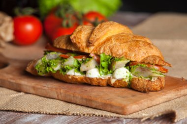 Kruvasan sandviç üzerinde ahşap kurulunda görev yapmaktadır. Kruvasan yumurta, eritilmiş peynir, maydanoz, tavuk jambon, füme somon ile