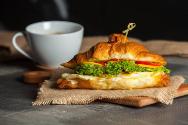Kruvasan sandviç üzerinde ahşap kurulunda görev yapmaktadır. Kruvasan yumurta, eritilmiş peynir, maydanoz, tavuk jambon, füme somon ile