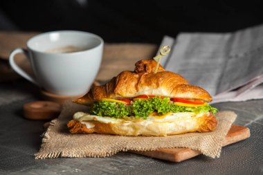Kruvasan sandviç üzerinde ahşap kurulunda görev yapmaktadır. Kruvasan yumurta, eritilmiş peynir, maydanoz, tavuk jambon, füme somon ile
