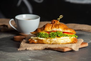 Kruvasan sandviç üzerinde ahşap kurulunda görev yapmaktadır. Kruvasan yumurta, eritilmiş peynir, maydanoz, tavuk jambon, füme somon ile