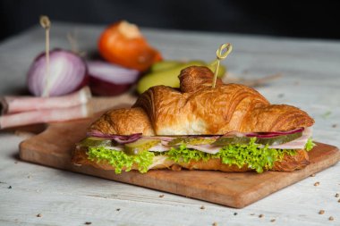 Kruvasan sandviç üzerinde ahşap kurulunda görev yapmaktadır. Kruvasan yumurta, eritilmiş peynir, maydanoz, tavuk jambon, füme somon ile