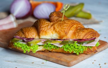Kruvasan sandviç üzerinde ahşap kurulunda görev yapmaktadır. Kruvasan yumurta, eritilmiş peynir, maydanoz, tavuk jambon, füme somon ile