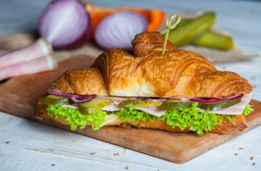 Kruvasan sandviç üzerinde ahşap kurulunda görev yapmaktadır. Kruvasan yumurta, eritilmiş peynir, maydanoz, tavuk jambon, füme somon ile