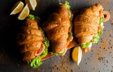 Kruvasan sandviç üzerinde ahşap kurulunda görev yapmaktadır. Kruvasan yumurta, eritilmiş peynir, maydanoz, tavuk jambon, füme somon ile