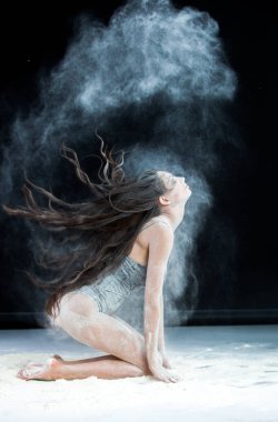 Zarif genç güzel seksi esmer toz bulutu içinde dans uzun saçlı. Toz siyah arka plan üzerine portre genç güzel seksi esmer kadın ile kaplı