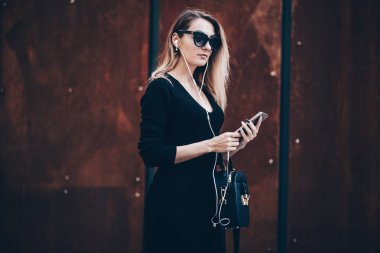 Cep telefonu tutan güzel bir iş kadını resmi. Sokakta duran ve cep telefonu kullanan genç bir kadın. Telefonla müzik dinleyen bir kadın.