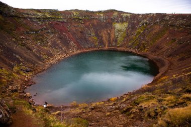 İzlanda 'daki Kerid volkanik krater gölü. Kerid Krateri 'nin tepesinde kırmızı volkanik taşlar ve İzlanda' da mavi krater gölü olan manzara.