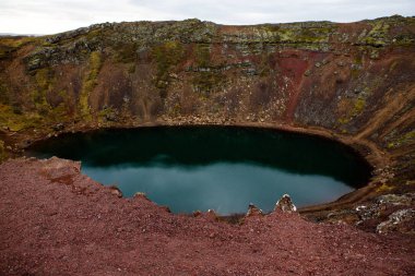 İzlanda 'daki Kerid volkanik krater gölü. Kerid Krateri 'nin tepesinde kırmızı volkanik taşlar ve İzlanda' da mavi krater gölü olan manzara.