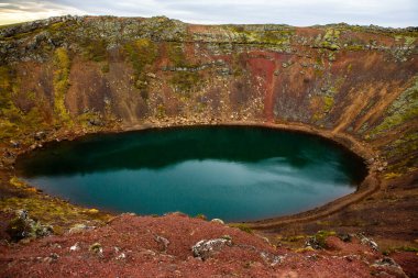 İzlanda 'daki Kerid volkanik krater gölü. Kerid Krateri 'nin tepesinde kırmızı volkanik taşlar ve İzlanda' da mavi krater gölü olan manzara.
