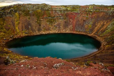 İzlanda 'daki Kerid volkanik krater gölü. Kerid Krateri 'nin tepesinde kırmızı volkanik taşlar ve İzlanda' da mavi krater gölü olan manzara.