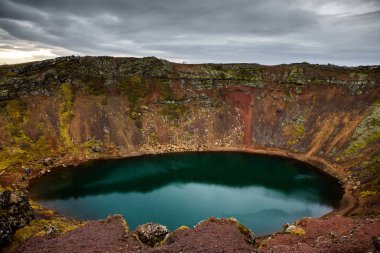 İzlanda 'daki Kerid volkanik krater gölü. Kerid Krateri 'nin tepesinde kırmızı volkanik taşlar ve İzlanda' da mavi krater gölü olan manzara.