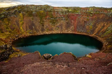 İzlanda 'daki Kerid volkanik krater gölü. Kerid Krateri 'nin tepesinde kırmızı volkanik taşlar ve İzlanda' da mavi krater gölü olan manzara.
