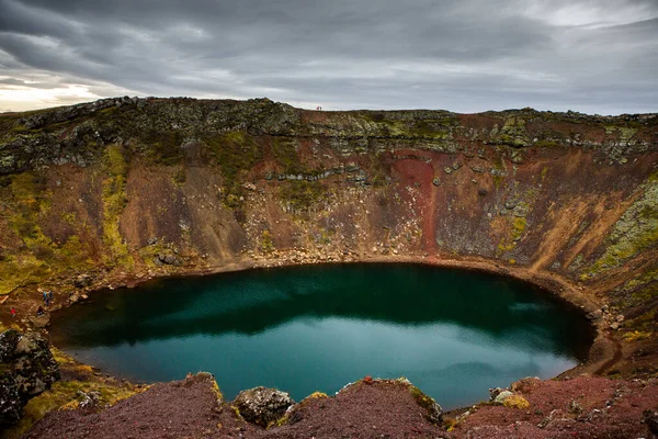 İzlanda 'daki Kerid volkanik krater gölü. Kerid Krateri 'nin tepesinde kırmızı volkanik taşlar ve İzlanda' da mavi krater gölü olan manzara.