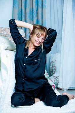 Genç güzel kadın ışık odada kirlenmiş. Rahat kadın pijamalar yatakta yatıyor. Günaydın kavramı - genç kadının uyanmanın mutlu gülümseme ile yüzünde.