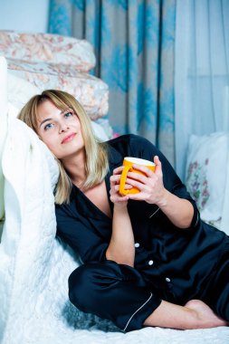 Genç güzel kadın ışık odada kirlenmiş. Rahat kadın pijamalar yatakta yatıyor. Günaydın kavramı - genç kadının uyanmanın mutlu gülümseme ile yüzünde.