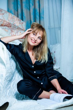 Genç güzel kadın ışık odada kirlenmiş. Rahat kadın pijamalar yatakta yatıyor. Günaydın kavramı - genç kadının uyanmanın mutlu gülümseme ile yüzünde.